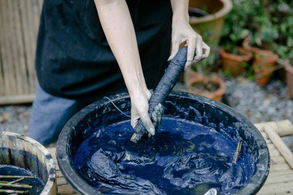 Hands dyeing textile fiber in a natural indigo dye vat
