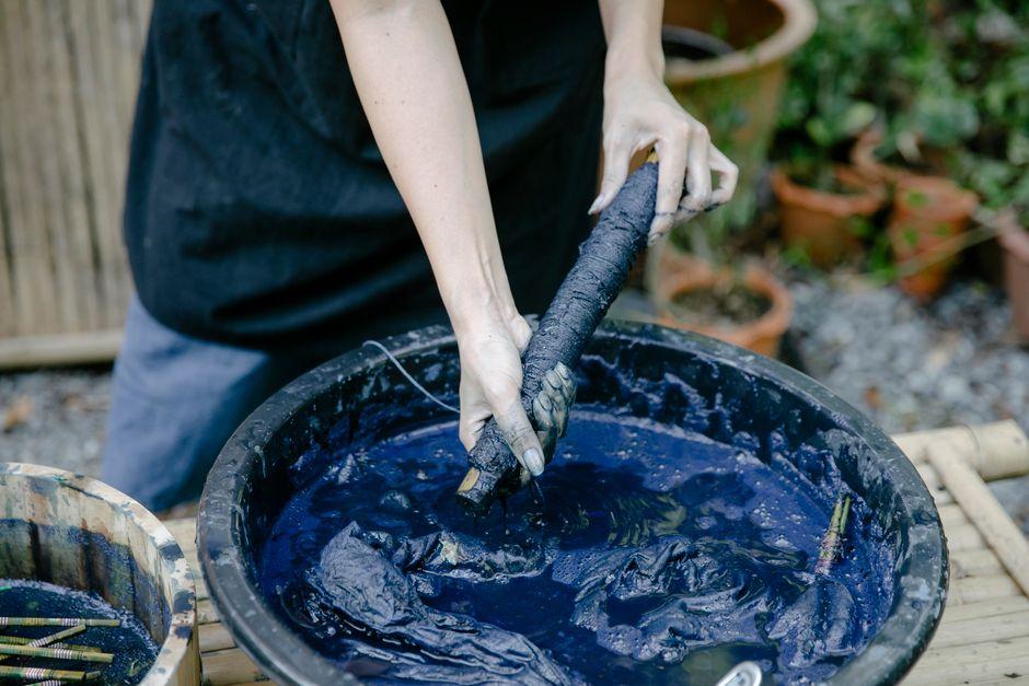 Hands dyeing textile fiber in a natural indigo dye vat
